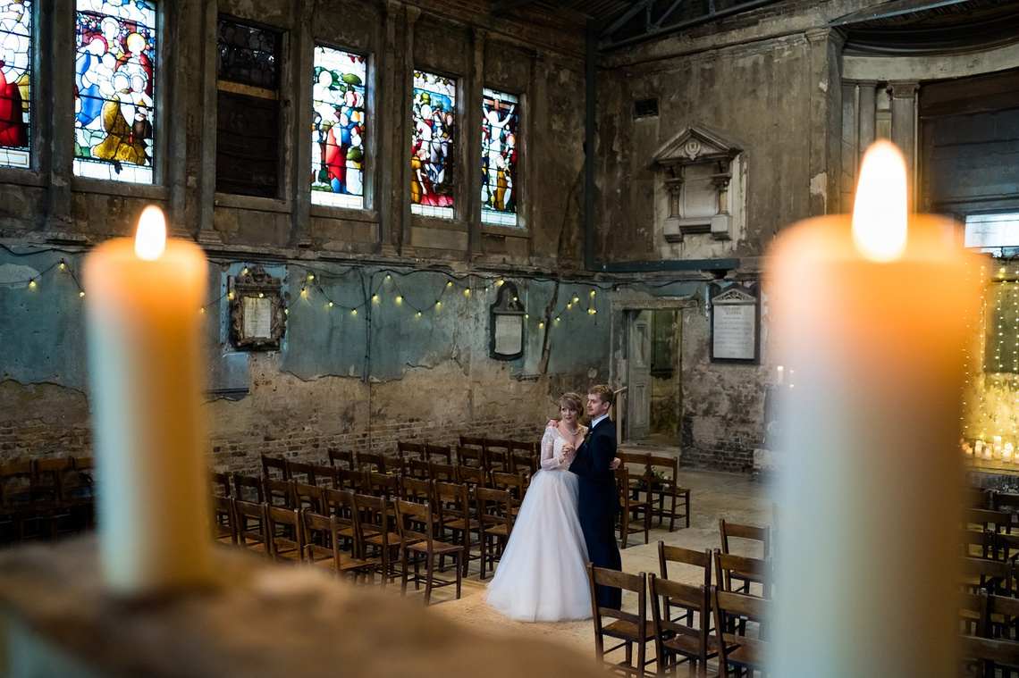 asylum wedding photographer, maverick project, cool and creative bride and groom photo between candles in decaying church peckham london