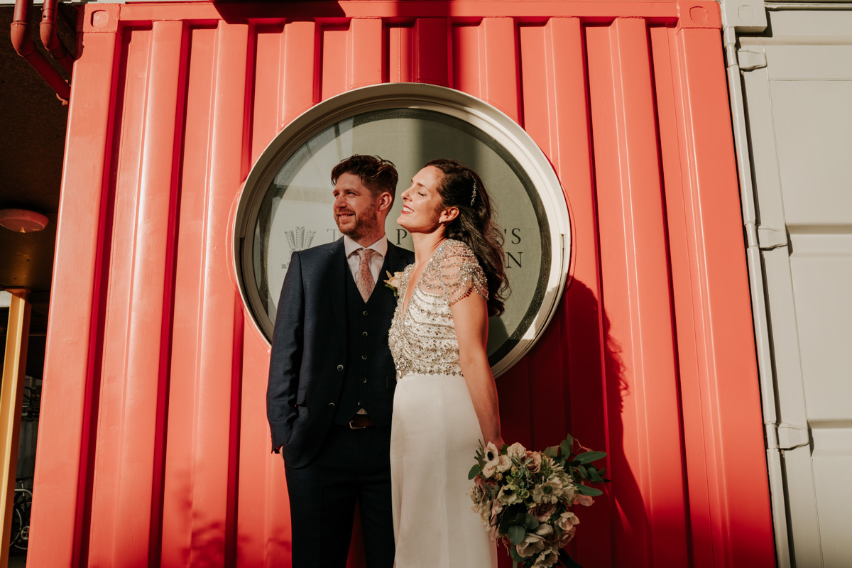 bride and groom basking in sun in front of orange sea container at trinity buoy wharf
