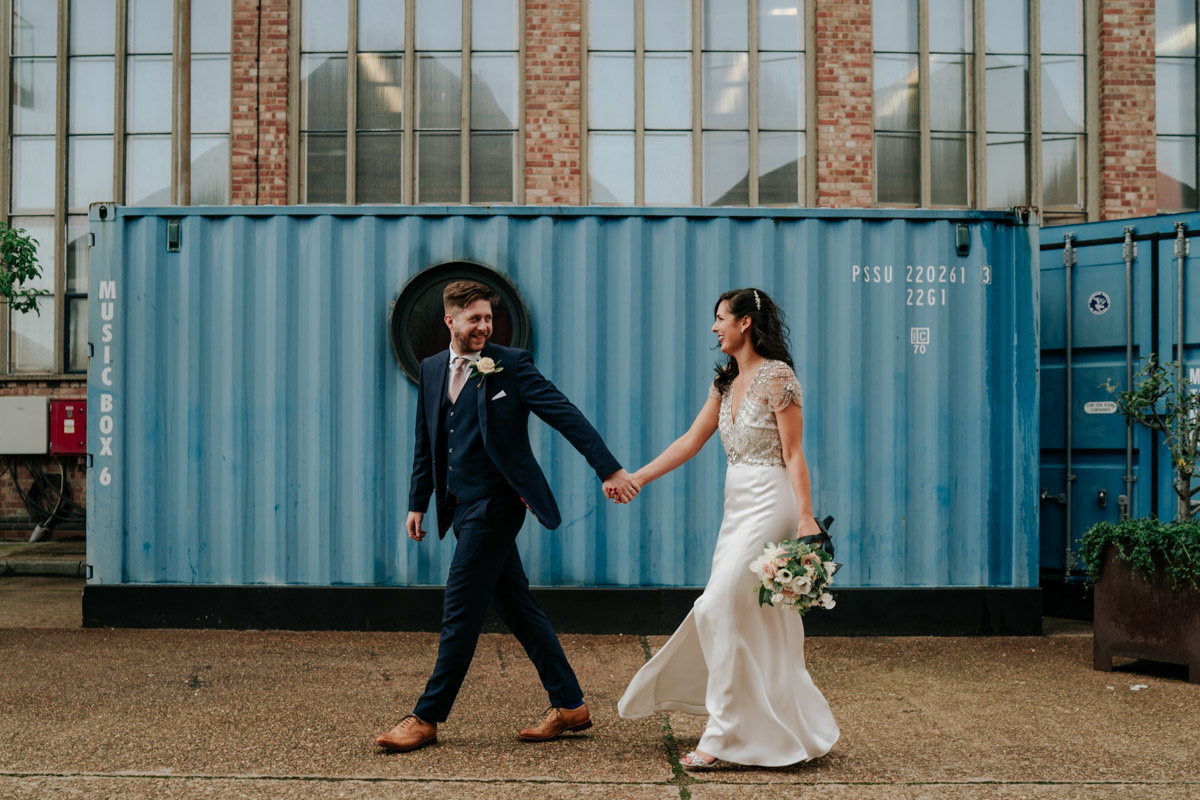bride and groom walking holding hands in front of sea containers at trinity buoy wharf