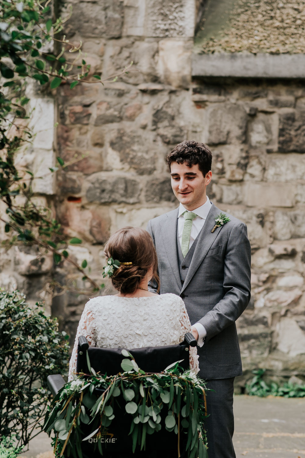 groom looking at his bride in a wheelchair decorated with foliage