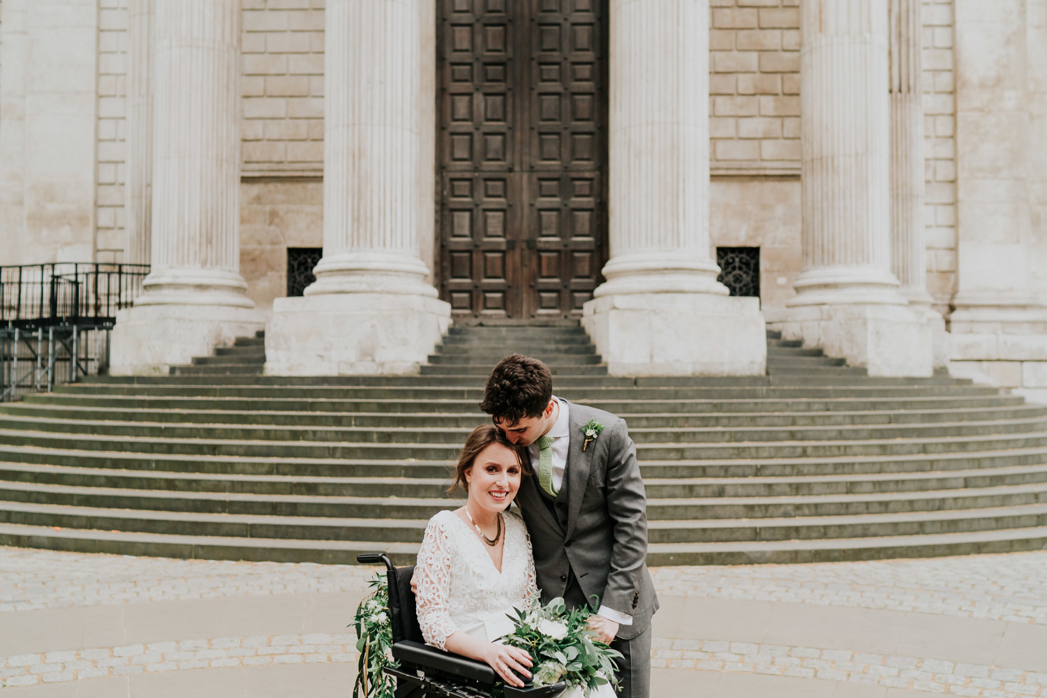 bride in a wheelchair smiling and groom kissing her hair