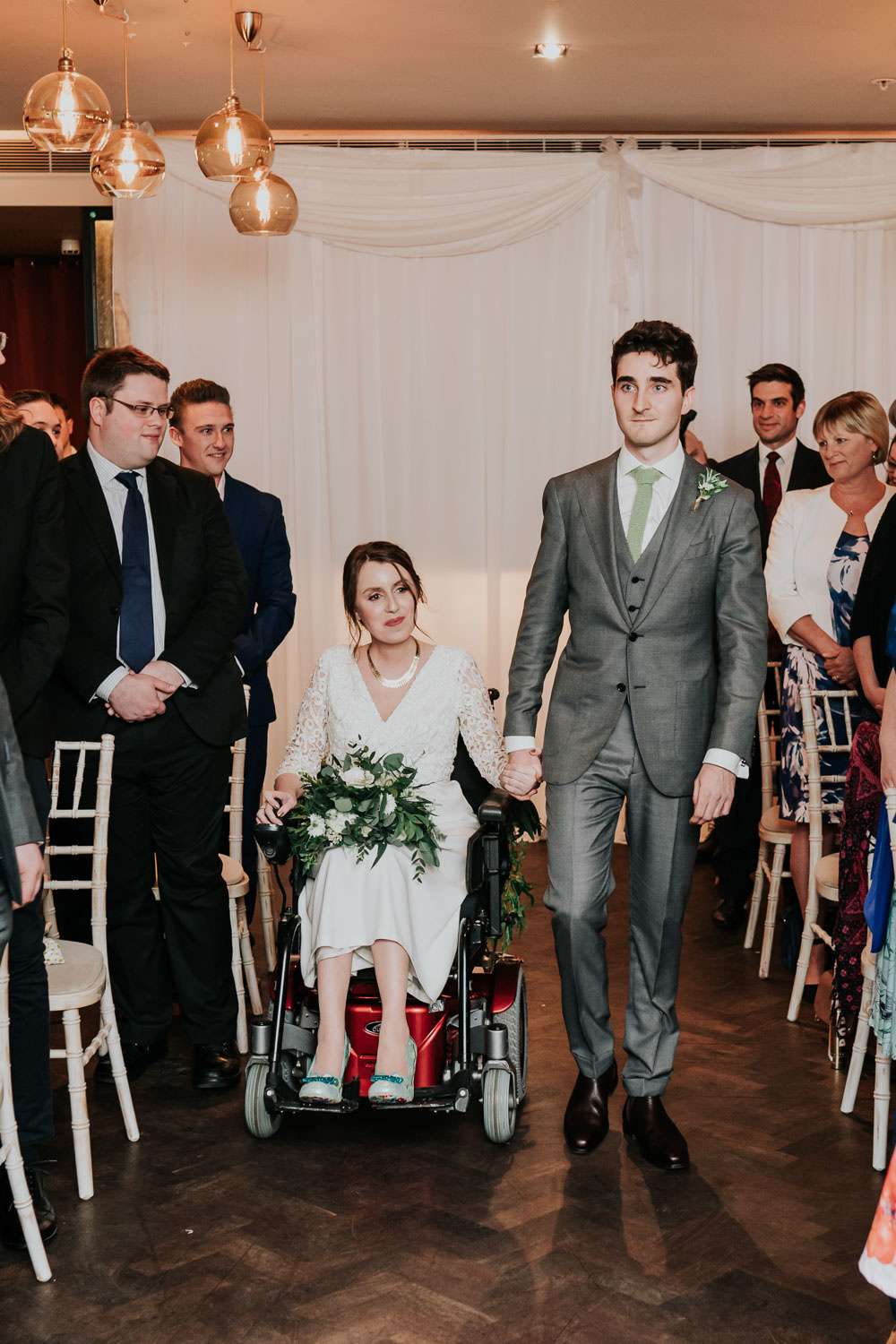 disabled bride in a wheelchair arriving at wedding ceremony holding grooms hand