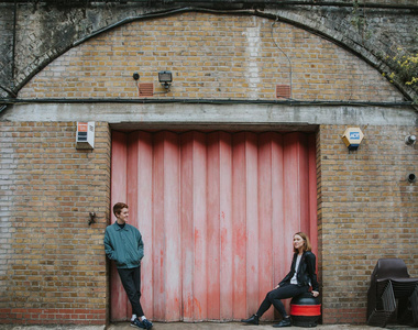 quirky london engagement photo with red shutters and couple looking away in Peckham near the asylum chapel