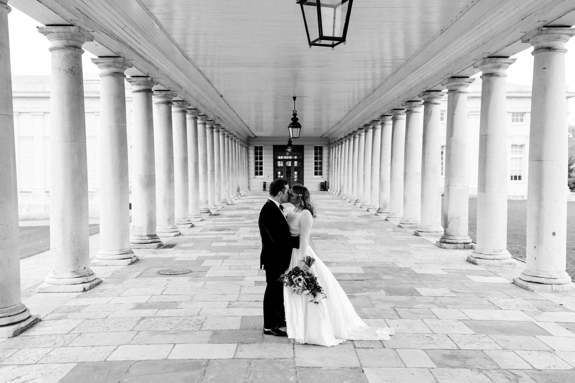 bride and groom kissing in a colonnade