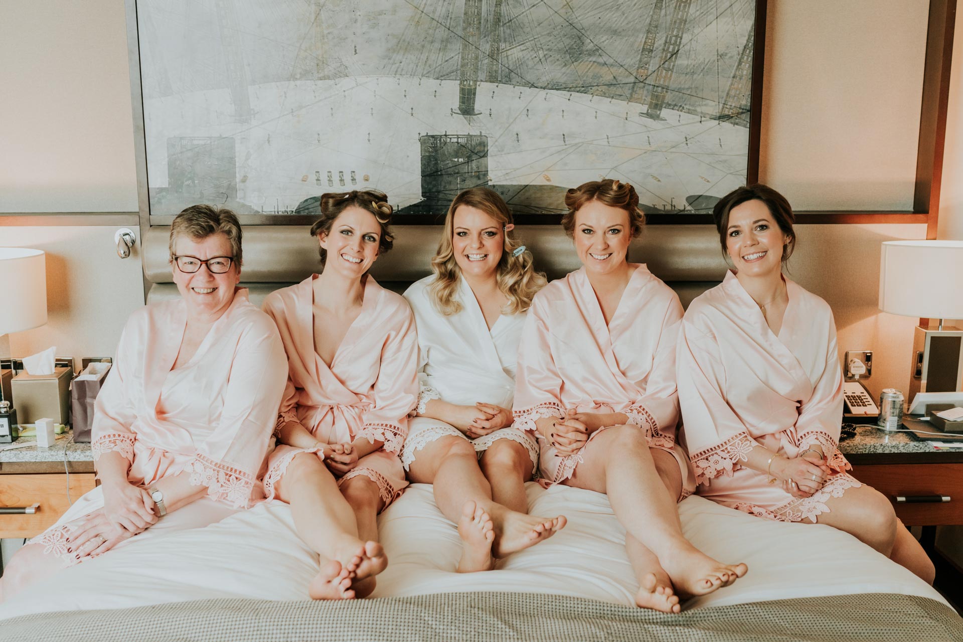 bride and bridesmaids in matching bathrobes on a bed in a hotel