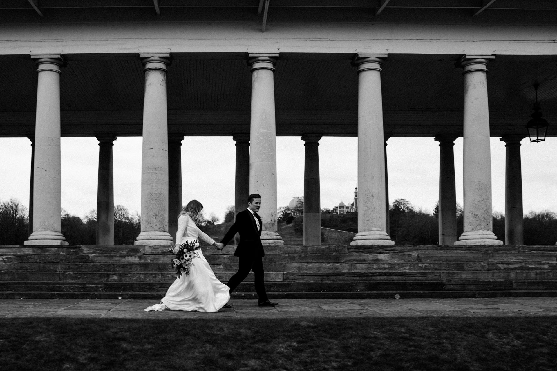 bride and groom walking near colonnade at queens house