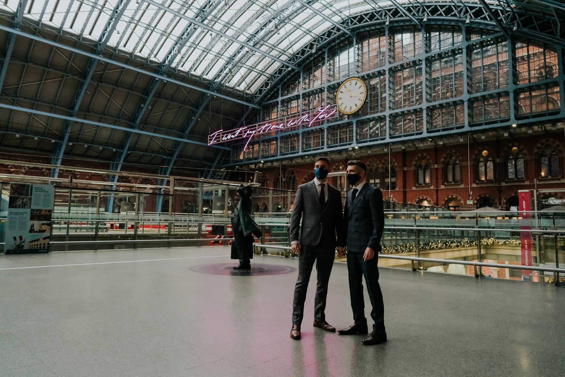 two grooms with masks posing at st pancras station
