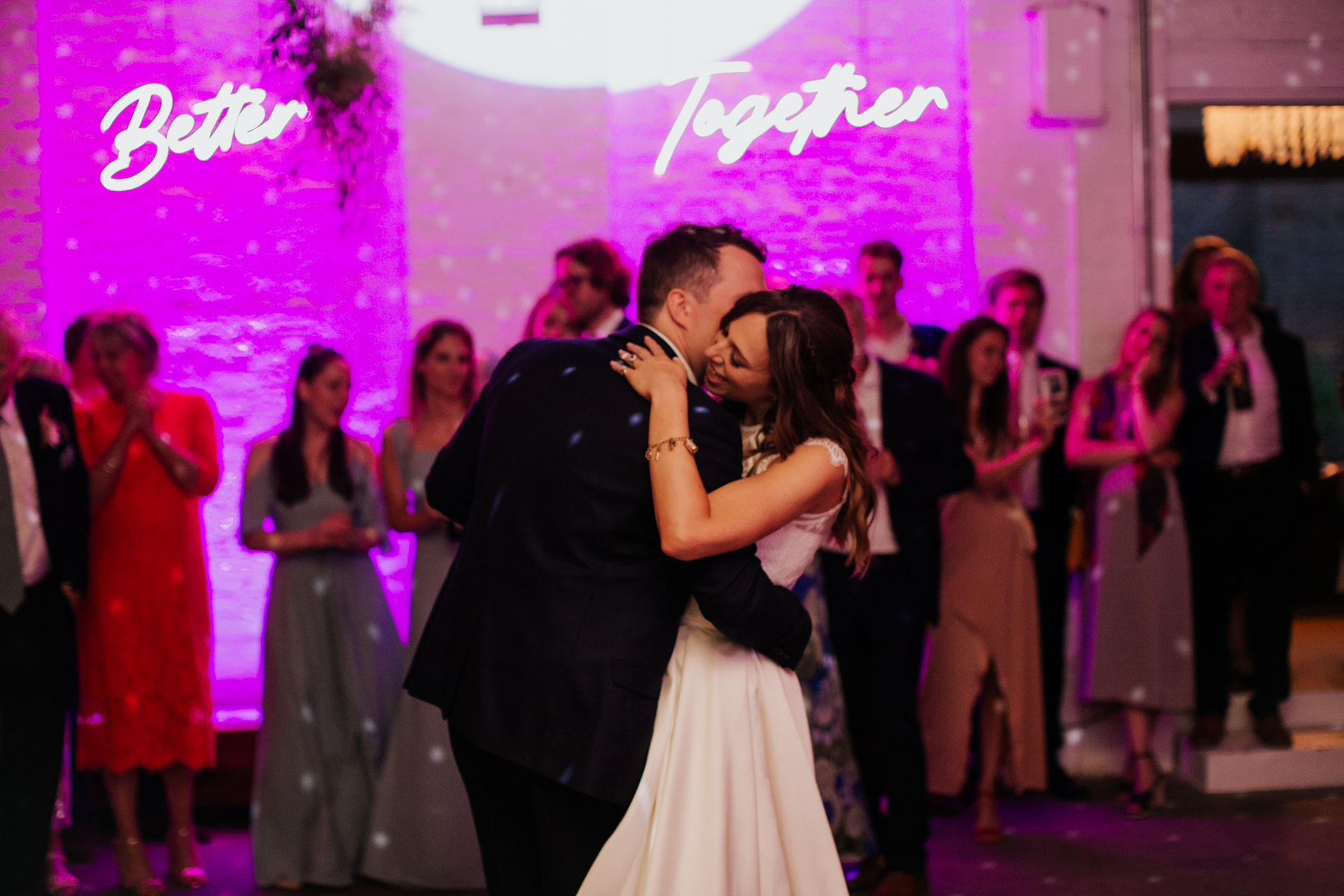 first dance photo of bride and groom with a neon sign saying better together behind them in 100 barrington wedding venue