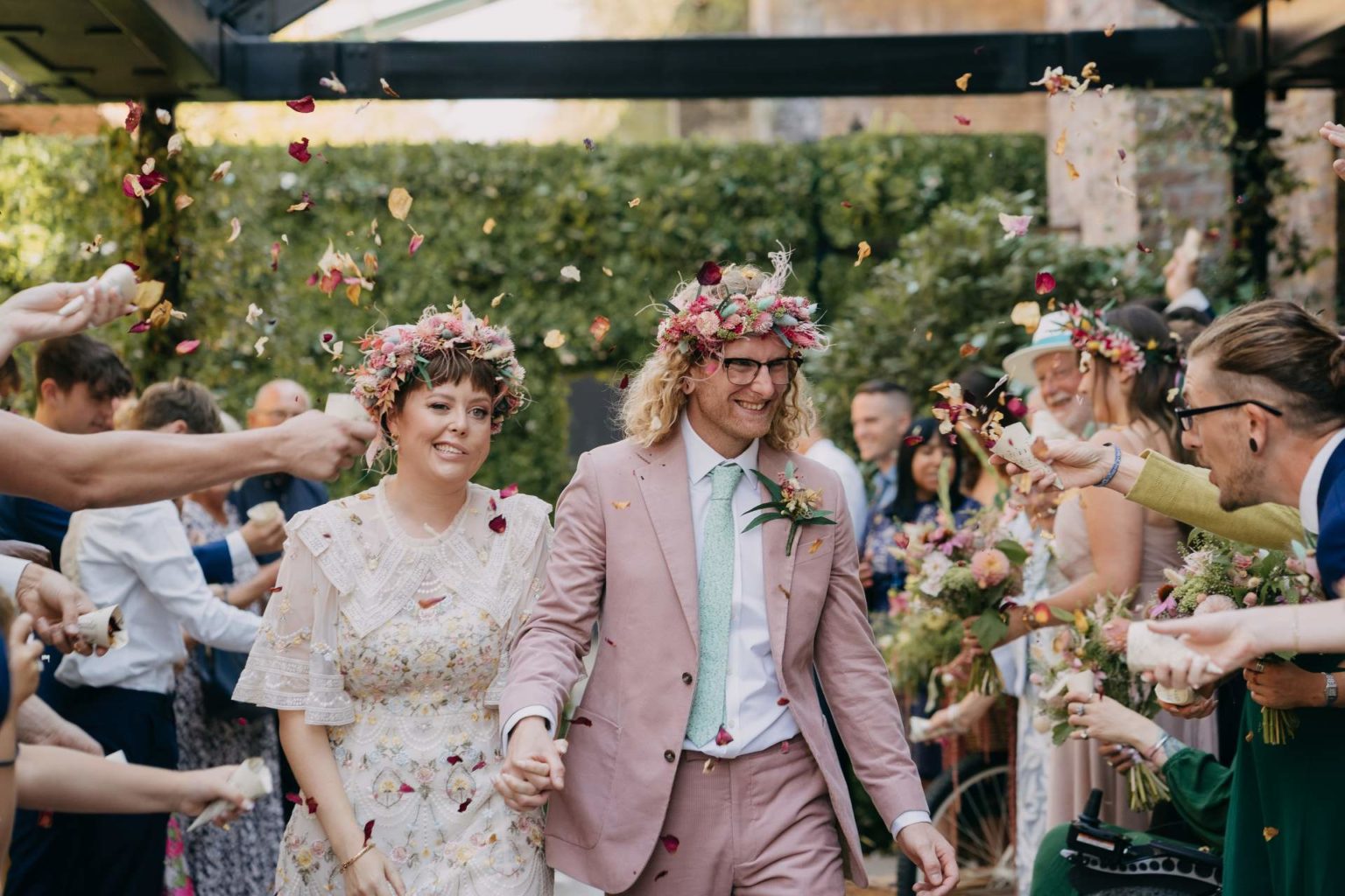 bride and groom smiling and holding hands walking through a confetti tunnel at 100 barrington road wedding venue