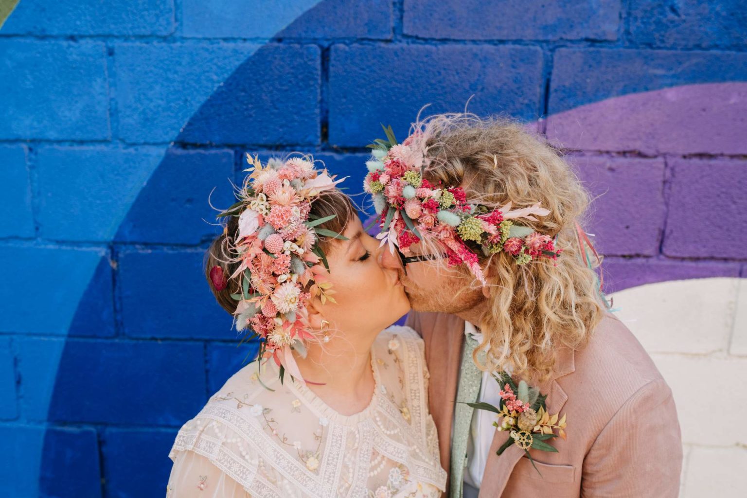 bride and groom with colourful flower crowns sharing a kiss in front of a vibrant backdrop of 100 barrington road venue