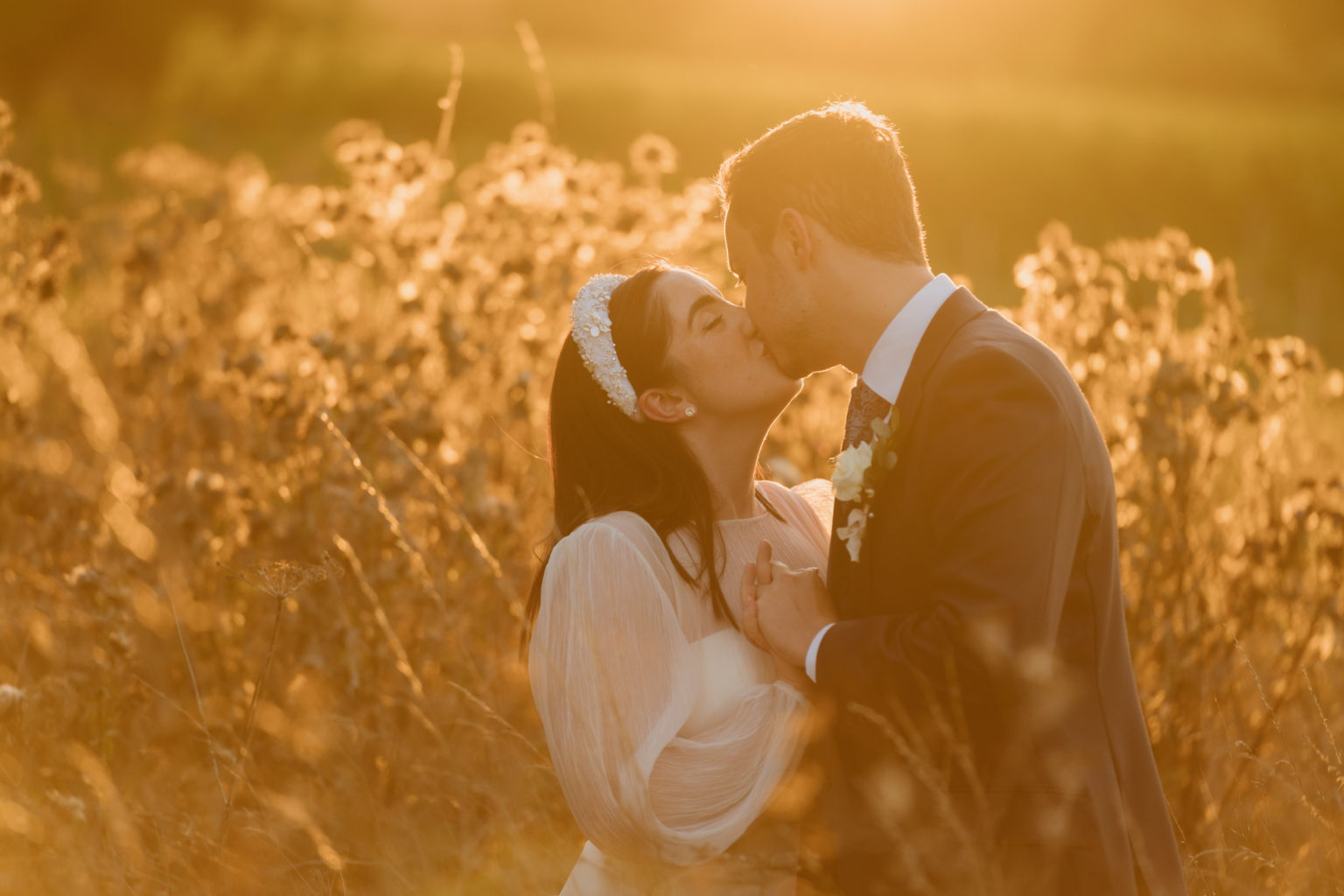 bride and groom kissing surrounded by tall dry grass and basked in sunset light at baddow park house