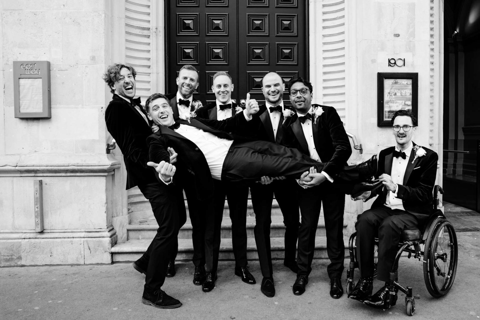 groom held by groomsmen and a wheelchair user in a funny pose outside andaz london hotel