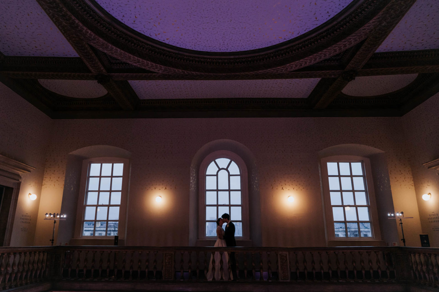 bride and groom kissing at dusk at queen's house balcony