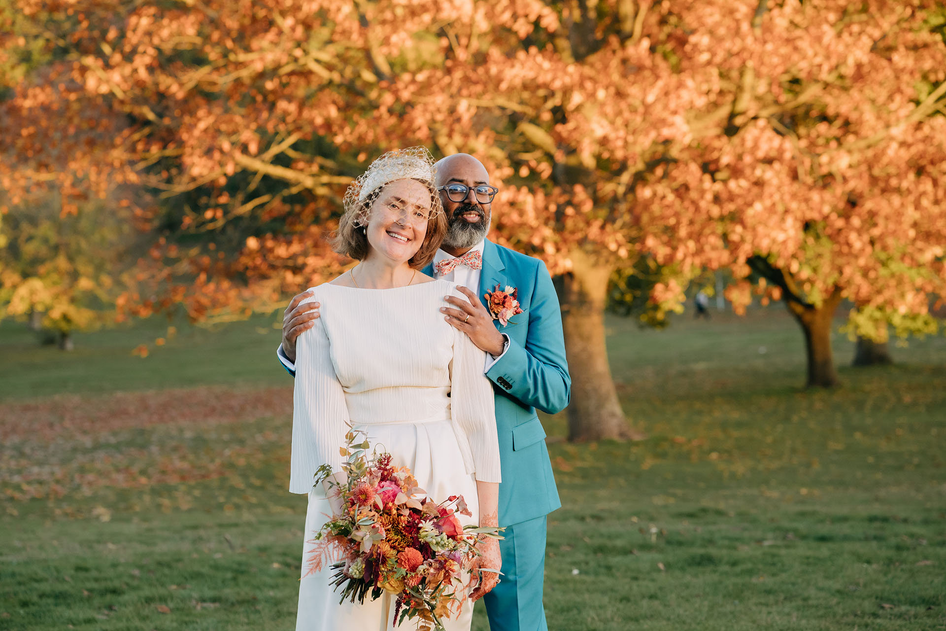 bride and groom in blue suit in front of autumn orange tree