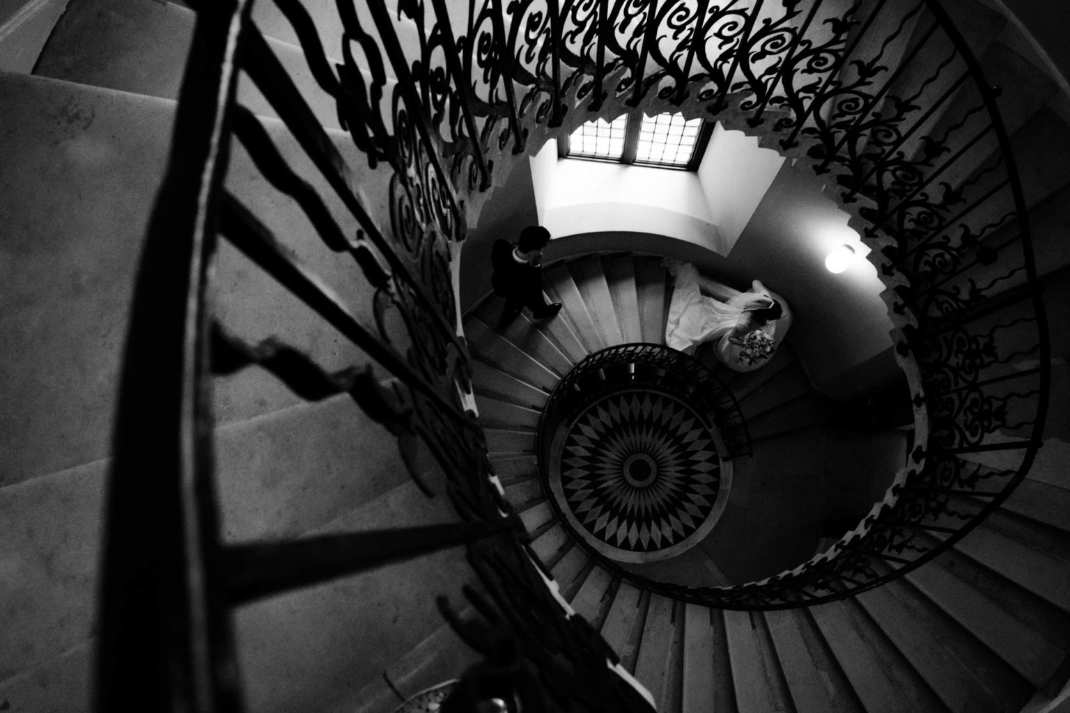 black and white photo of bride and groom walking down spiral staircase at queens house