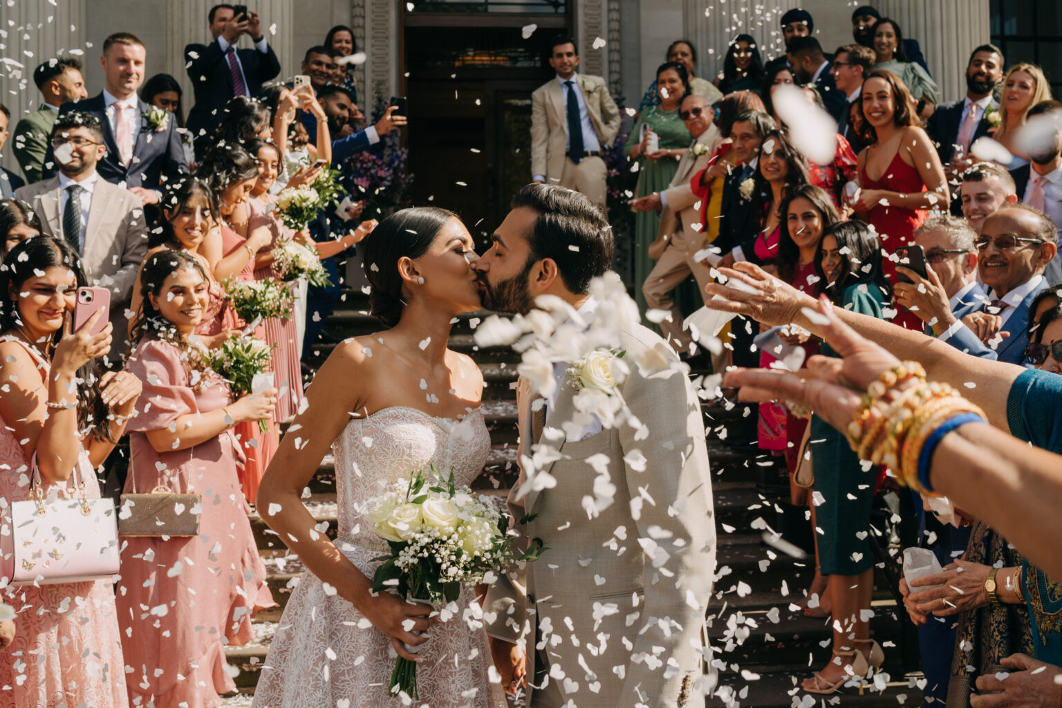 bride and groom kissing in confetti on the old marylebone town hall steps in sunshine