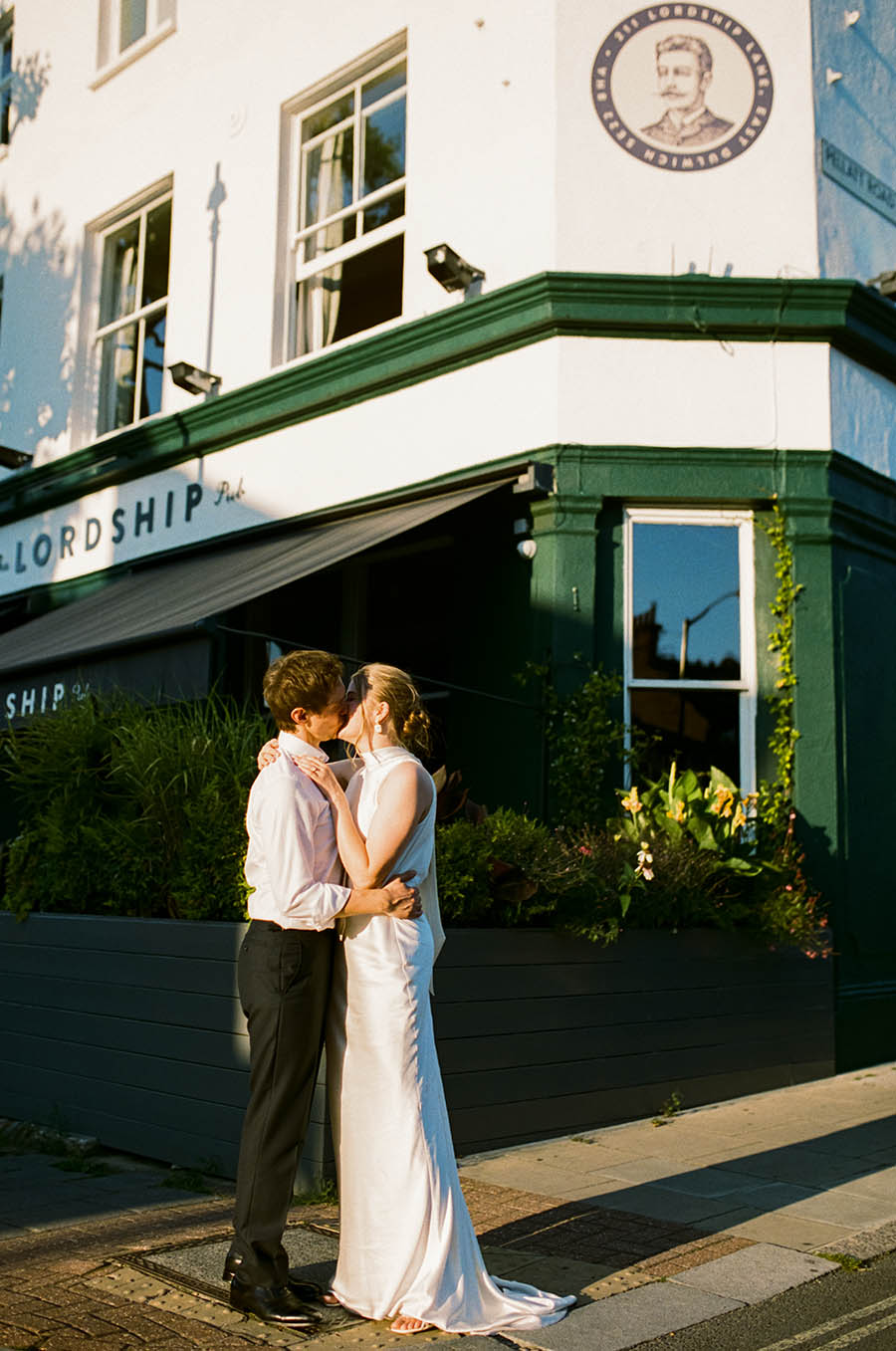 birde and groom kissing in golden hour sunlight outside the Lordship pub captured on portra film