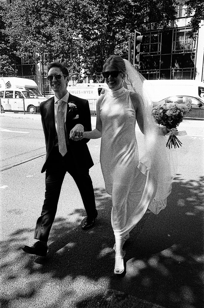 grainy film wedding photo of bride and groom walking london street