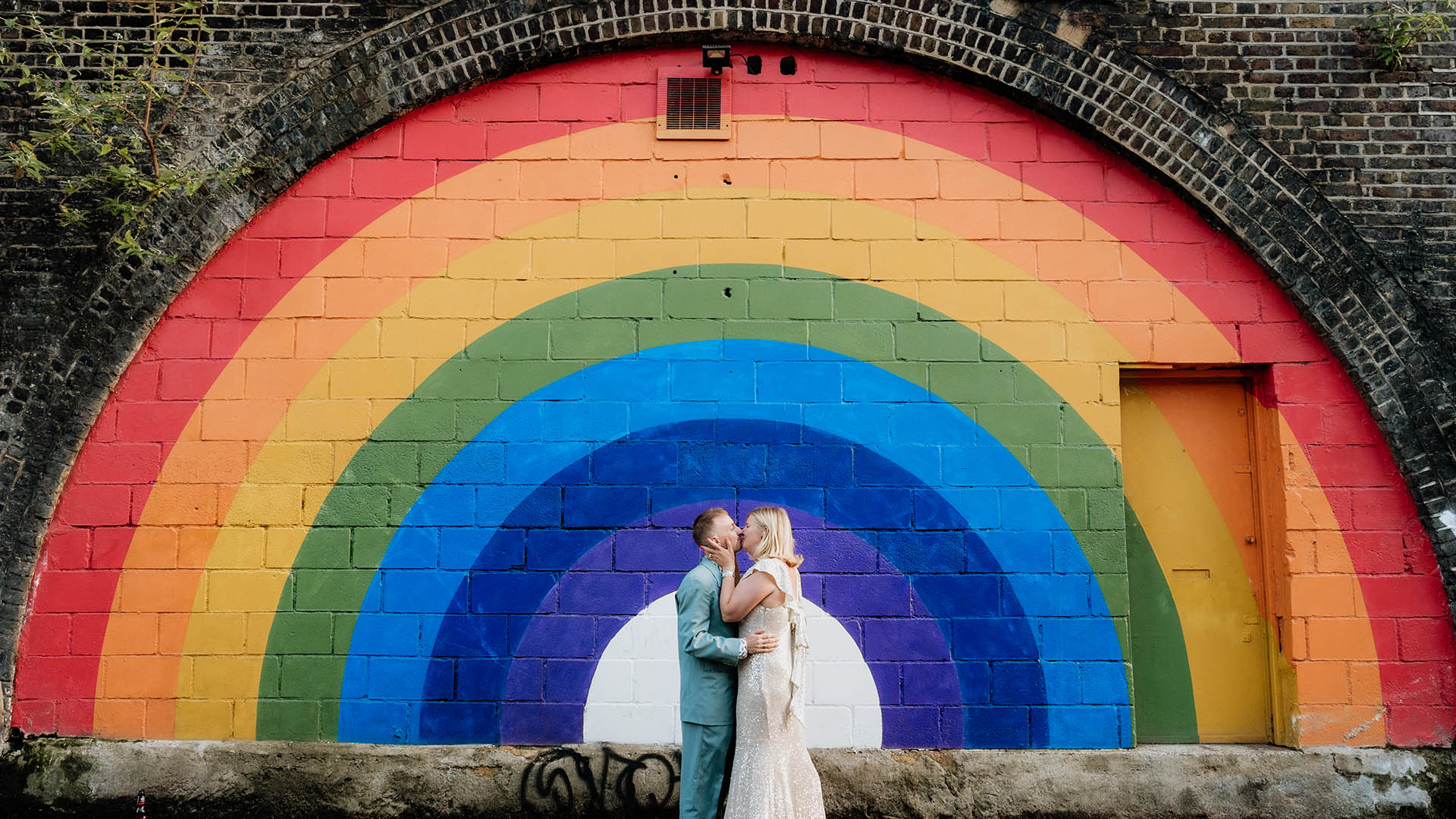 bride and groom kissing in front of rainbow mural at 100 barrington photo by joasis photography
