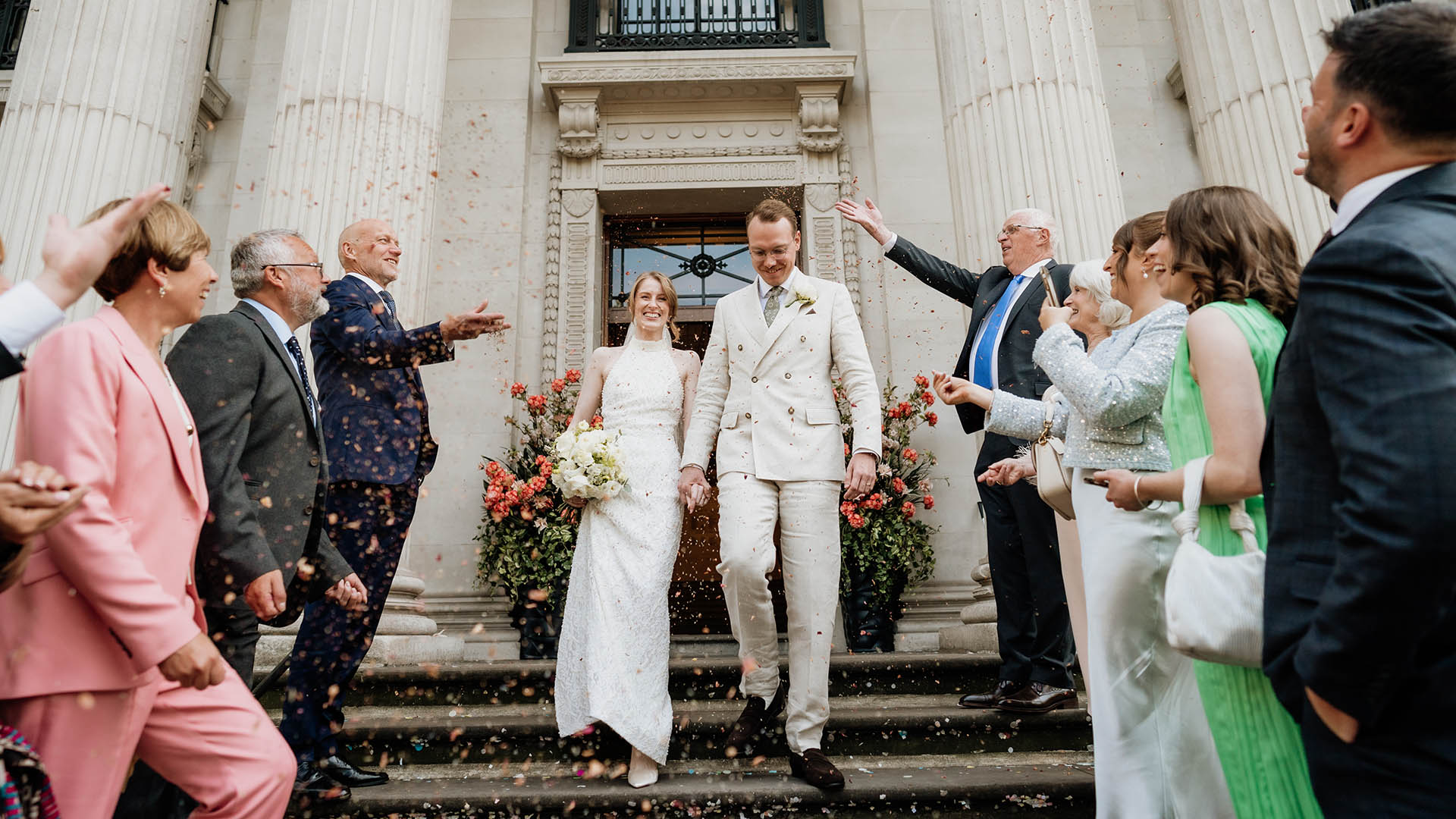 confetti exit at the old marylebone town hall by editorial wedding photographer, bride in white dress and groom in sand colour suit