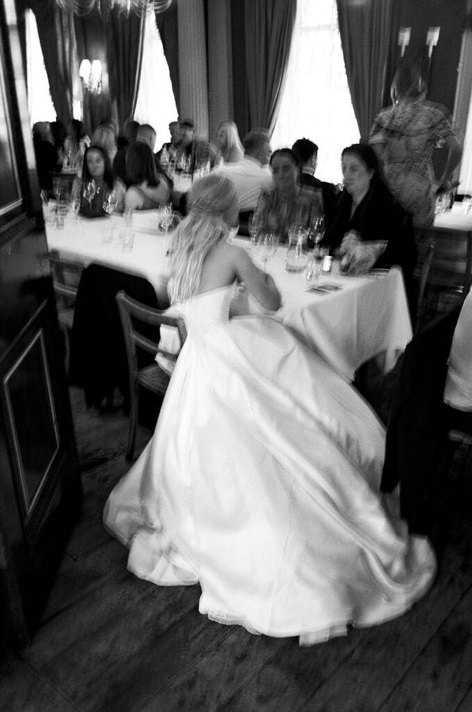 editorial, cinematic photo in black and white on 35mm film - blurry artistic candid photo of bride in a long dress sitting with guests at brunswick house weddin venue
