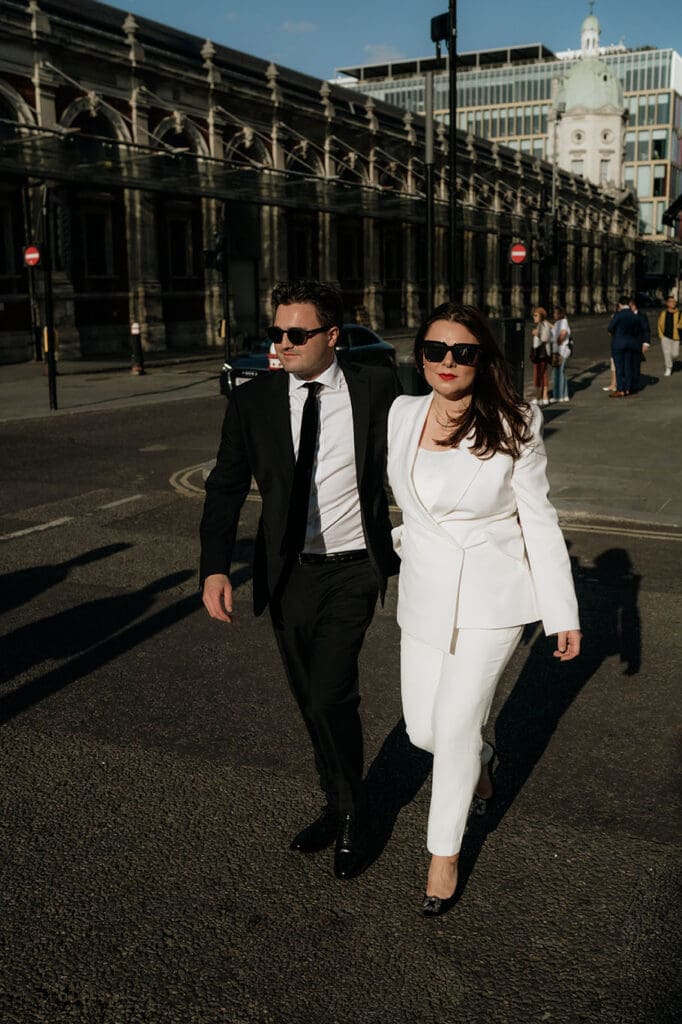 brride in white alexander mcqueen suit and groom in black suit, walking from balfour to smithfields, with sunglasses on
