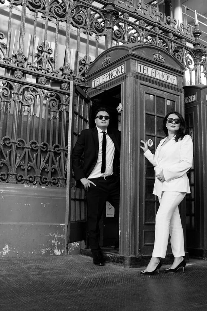 bride in white suit posing with groom in black tie suit with a telephone box at smithfields market after wedding at balfour