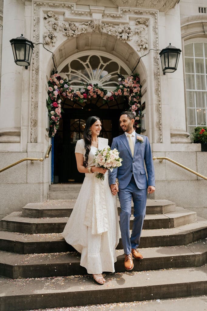 bride in asian sari and groom in blue suit on the steps of the chelsea town hall