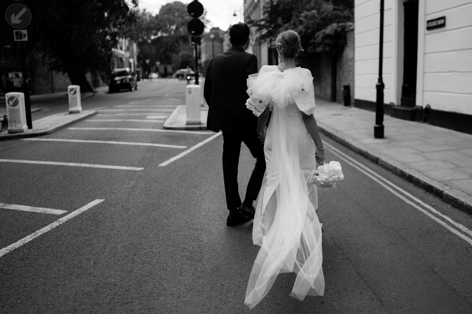 creative portrait of bride and groom walking away with their backs and long veil and bow on the wedding dress at the islington town hall