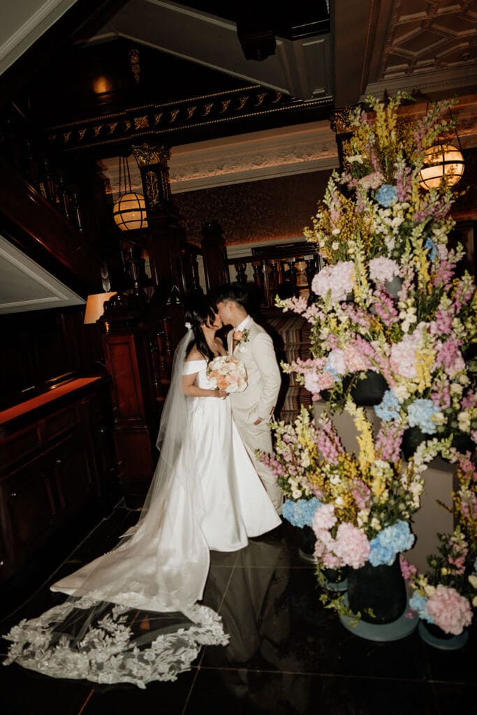 hard flash portrait of bride and groom kissing near florals at the connaught hotel