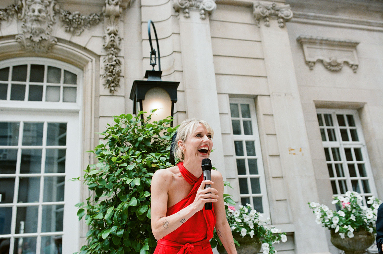 bridesmaid doing a standing wedding speech, woman in a red dress laughing