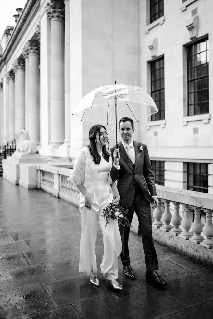 rainy wedding day natural walking couple photo with them holding a clear umbrella outside old Marylebone town hall 
