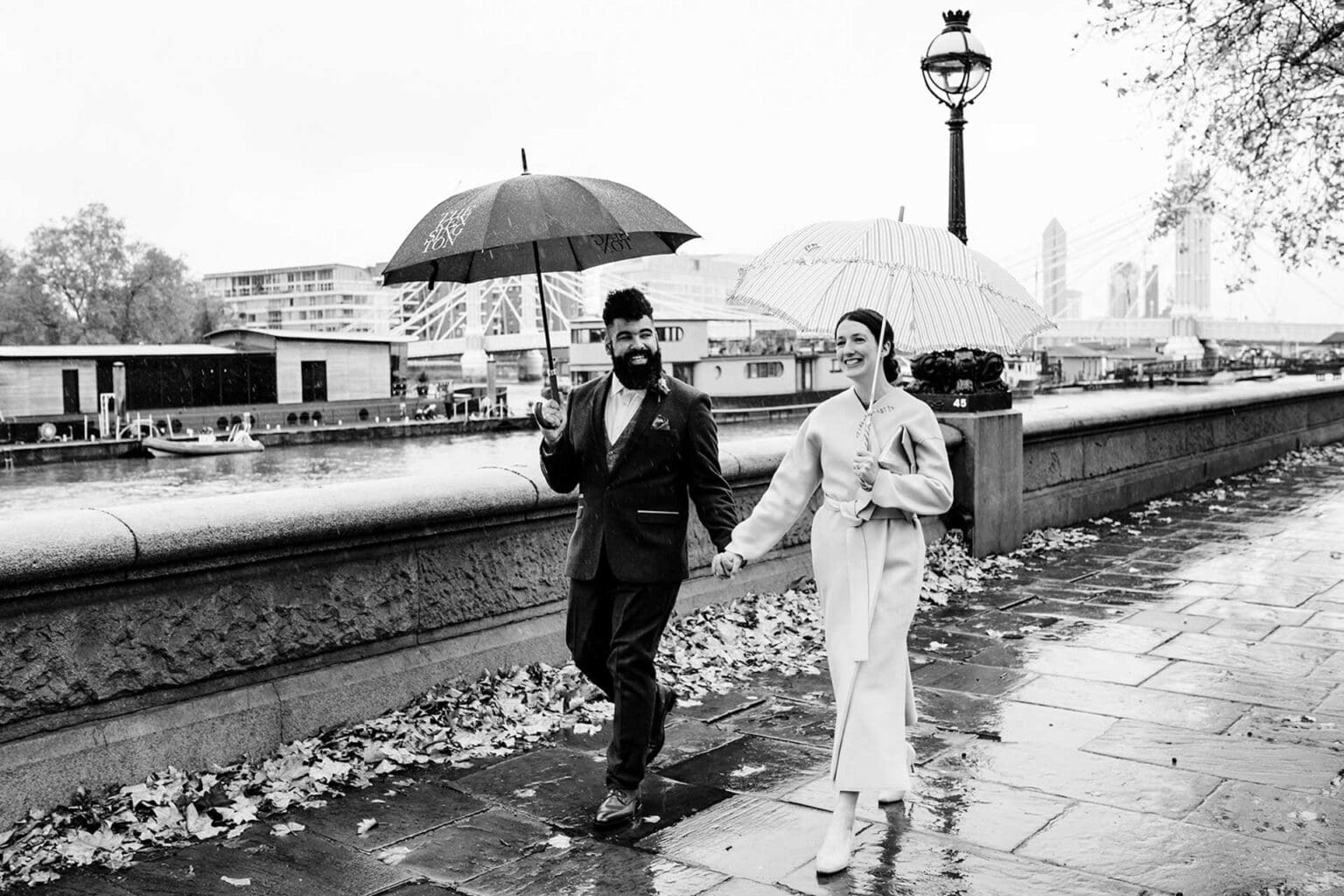 cinematic rainy wedding day photography with bride and groom walking and holding hands and umbrellas wrapped in warm coats