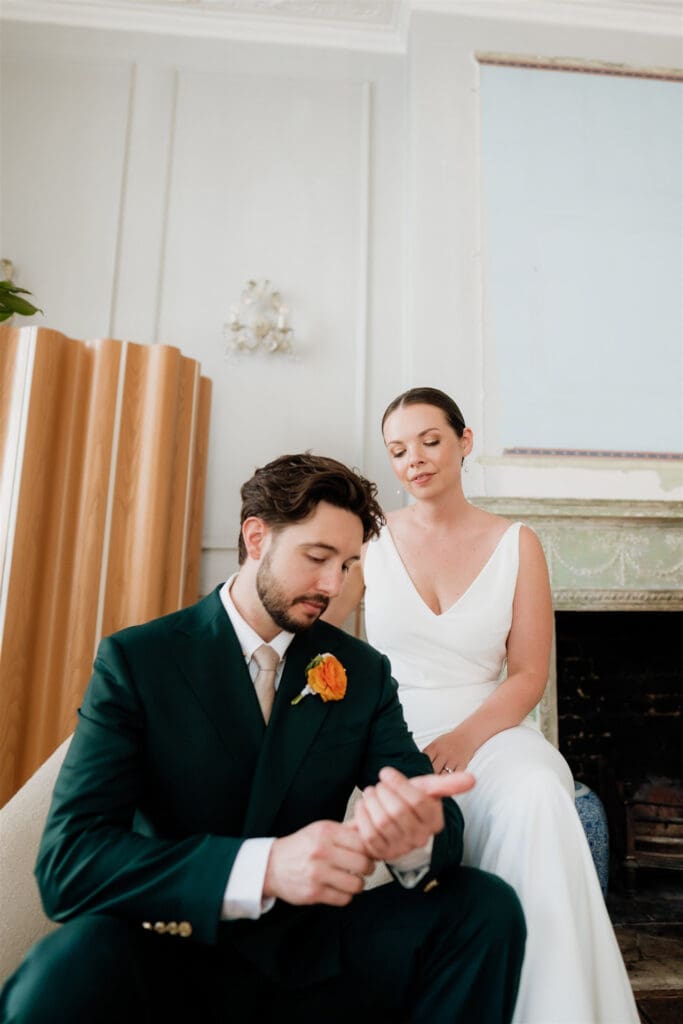 editorial wedding photo of groom sitting and looking at his hands and bride sitting on his chair behind