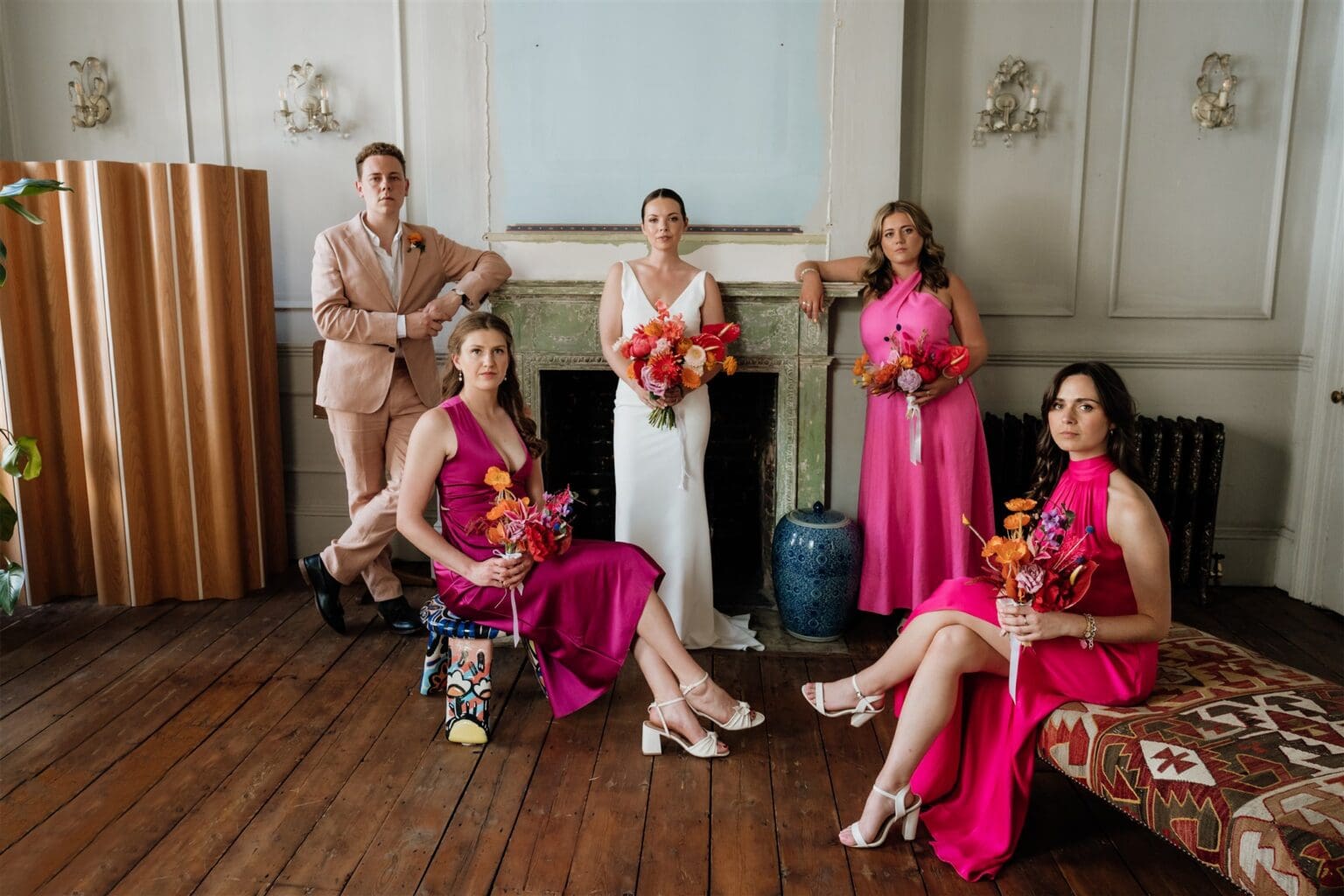 indoor editorial portrait of bridal party in pink outfits with pink and orange flowers, vogue like posing by wedding photographer london