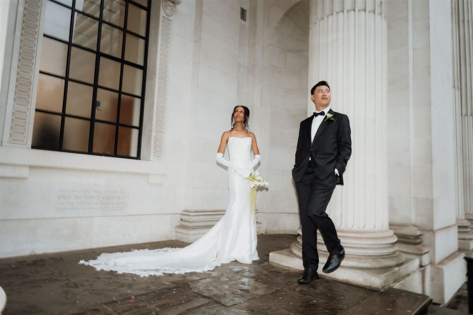 editorial wedding photography of bride in long white dress with gloves on and groom in black tie looking away under marylebone town hall canopy