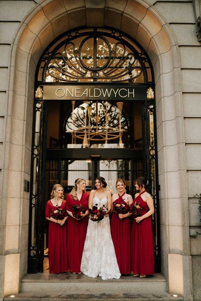 creative way to avoid rain on wedding day and pose under one aldwych hotel doorway, bride in white and bridesmaids in red dresses