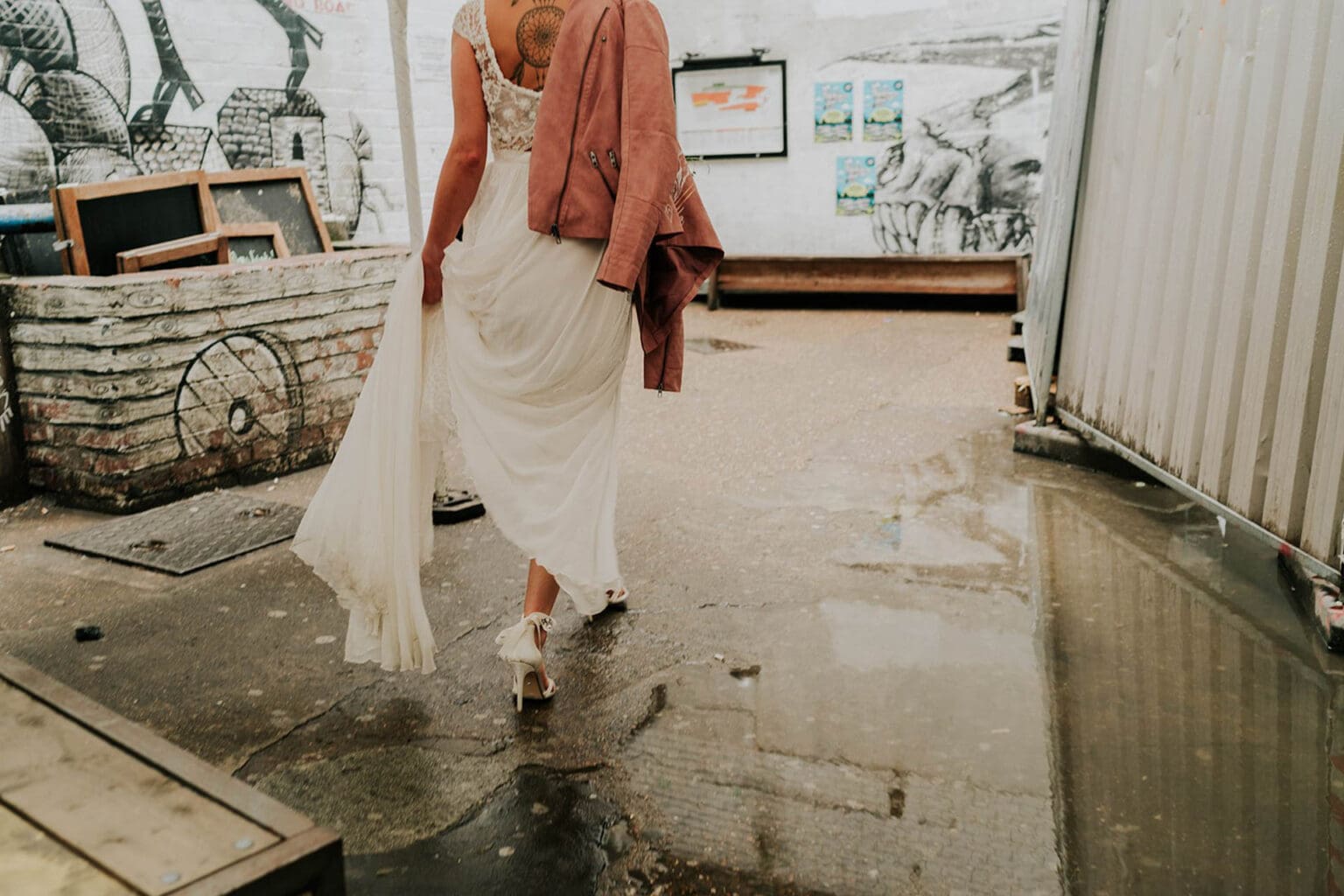 detailed artistic photo of bride from the back carrying wet wedding dress and walking through paddles in stilletos on a rainy wedding day in london