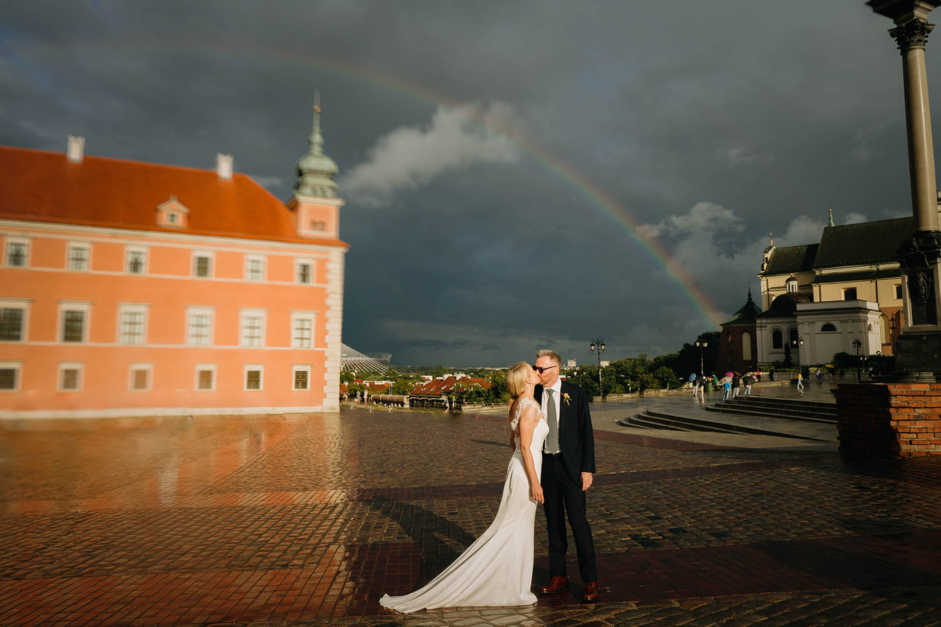 bride and groom basking in post rain sunshine with a rainbow behind