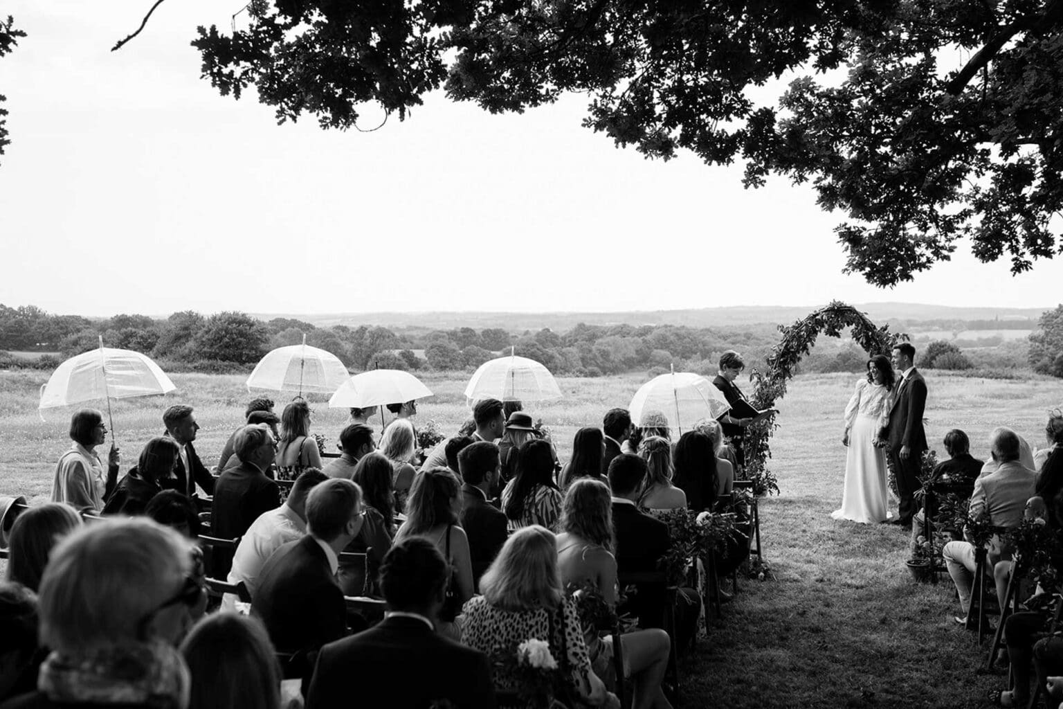 an outdoor ceremony with a rain on a wedding day with guests sheltering under clear dome umbrellas and couple still enjoying the day