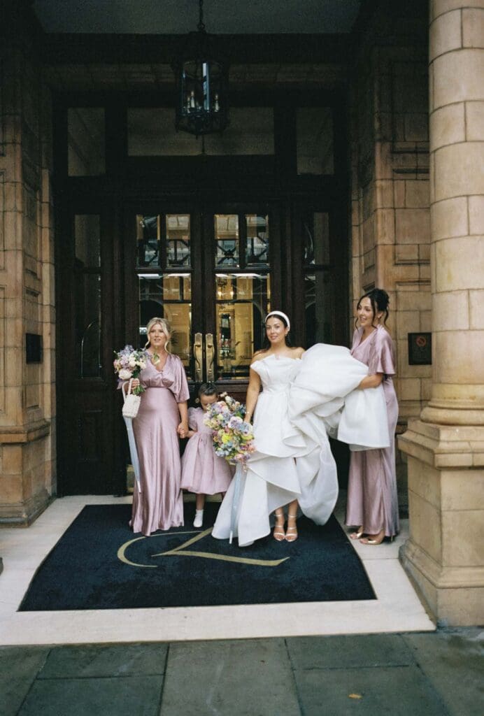bridesmaid holding bride's dress to protect from rain. film wedding photography on a rainy wedding day in london landmark hotel