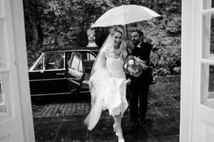 father shielding bride from rain with an umbrella, bride smiling and holding her dress