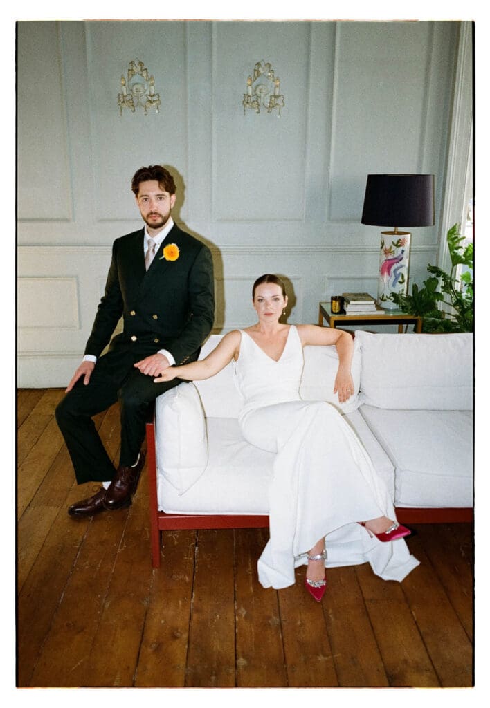 editorial wedding portrait of a couple sitting n a sofa and looking solemnly into camera taken on 35mm film, analogue grain texture