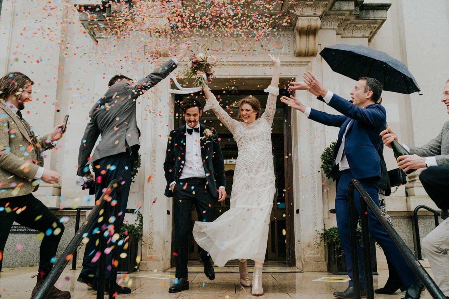 bride and groom cheering and leaving london town hall for a confetti in strong winds and rain on wedding day