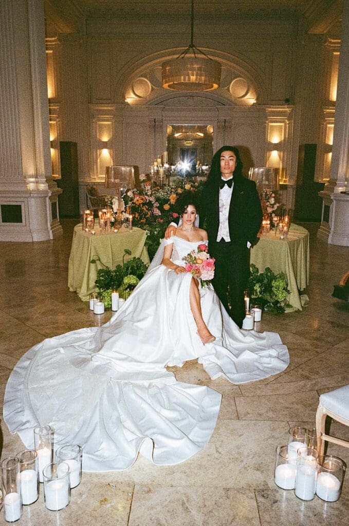Editorial film photo portrait of bride sitting with a long white dress and groom in black tux at andaz hotel in London