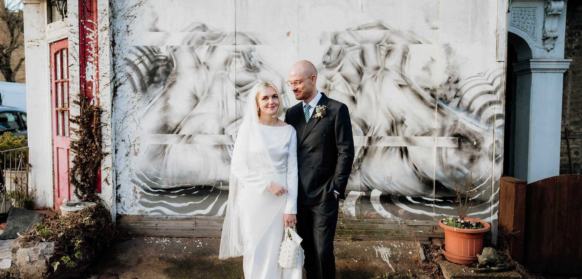 groom looks at bride in front of graffitti outside lordship pub wedding venue