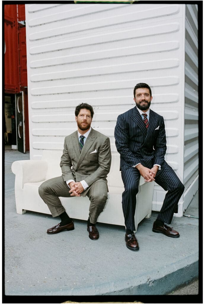 editorial wedding portait of two grooms sitting against white wall at trinity buoy wharf