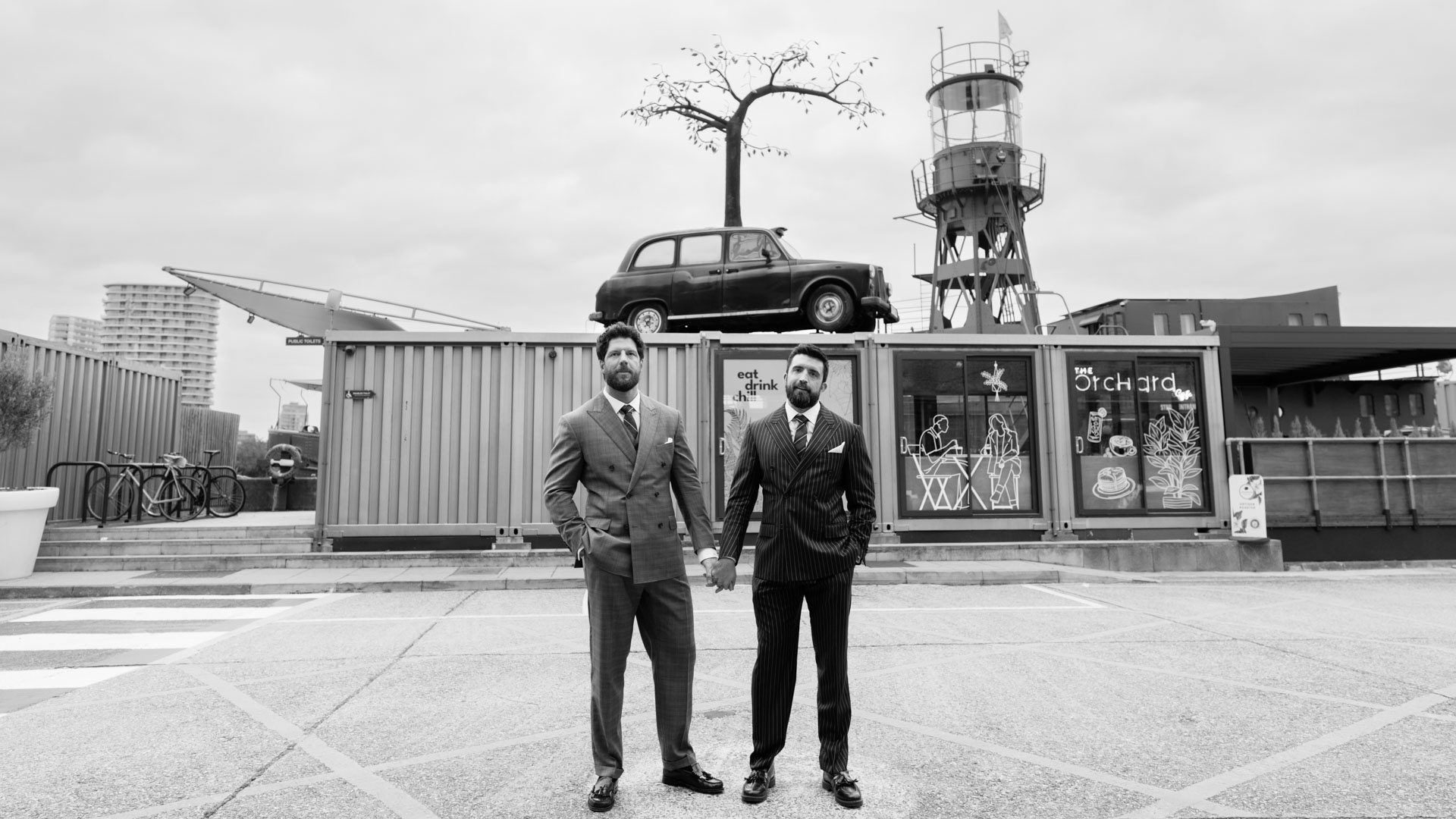 same sex couple posing in front of taxi sculture at trinity riverside london